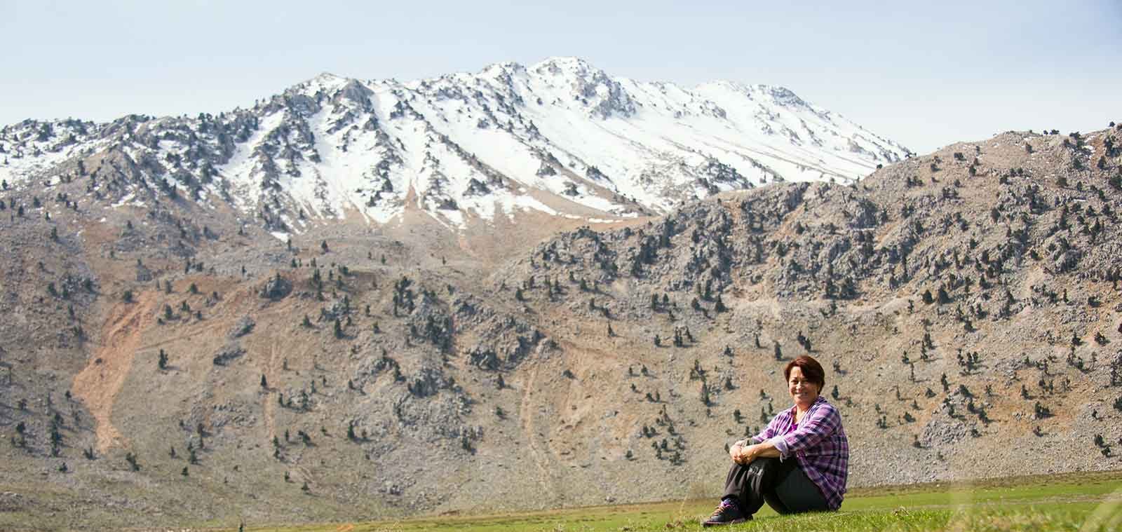 A snow-capped ridge of the western Taurus mountains above Antalya, with Yasemin Konuralp sitting on the spring turf at the foot of the slope.